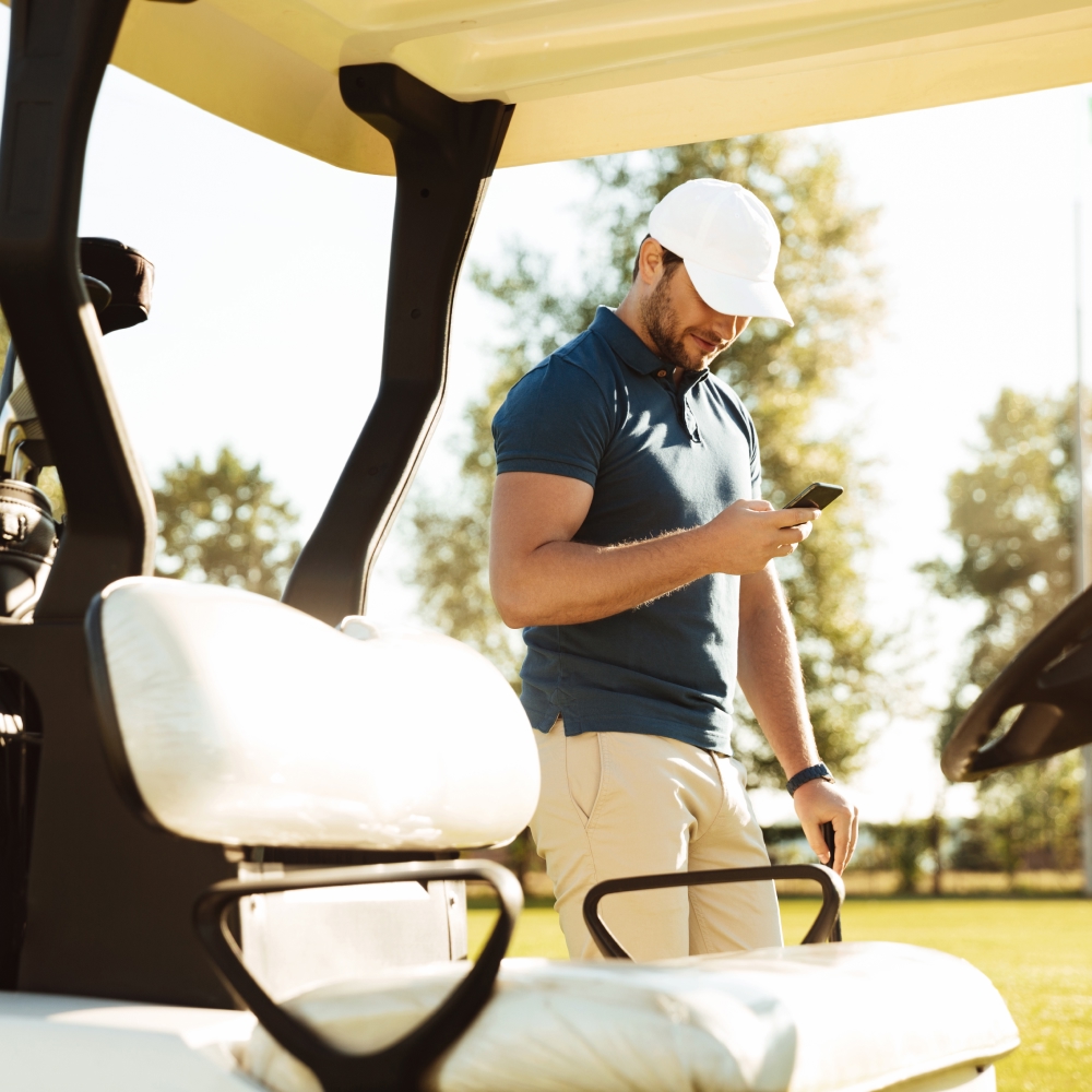 Man looking at smart phone next to a golf cart